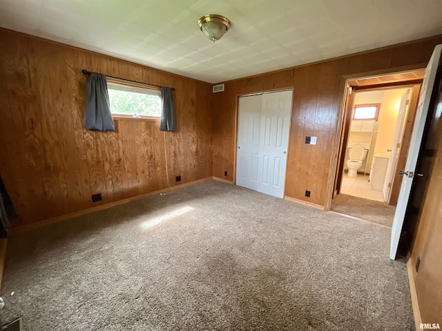 unfurnished bedroom with wooden walls, carpet flooring, baseboards, and visible vents