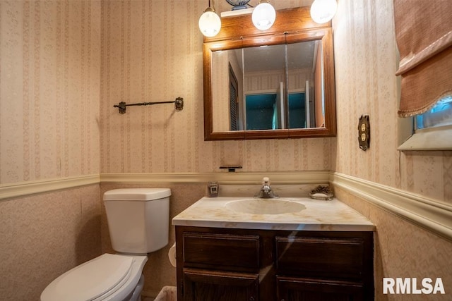 half bath featuring toilet, vanity, and wallpapered walls