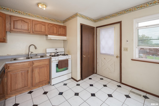 kitchen with under cabinet range hood, white gas range, visible vents, a sink, and light countertops