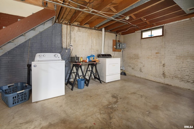 basement with brick wall, washer and dryer, and electric panel