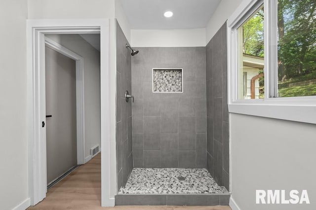bathroom with tiled shower, a healthy amount of sunlight, visible vents, and wood finished floors