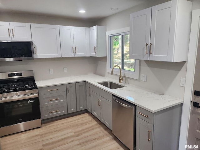 kitchen featuring gray cabinets, stainless steel appliances, light stone countertops, and a sink