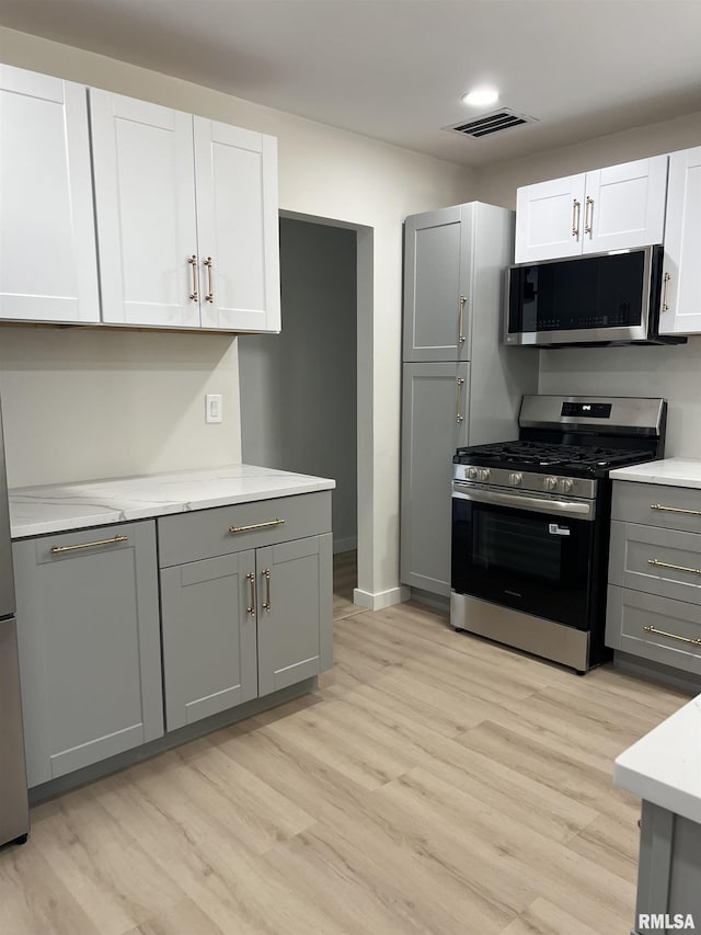 kitchen featuring light wood finished floors, visible vents, baseboards, gray cabinetry, and appliances with stainless steel finishes