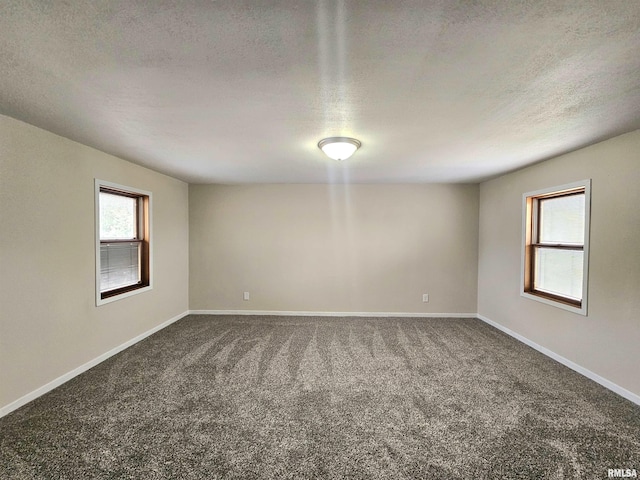 spare room featuring dark colored carpet, a textured ceiling, and baseboards