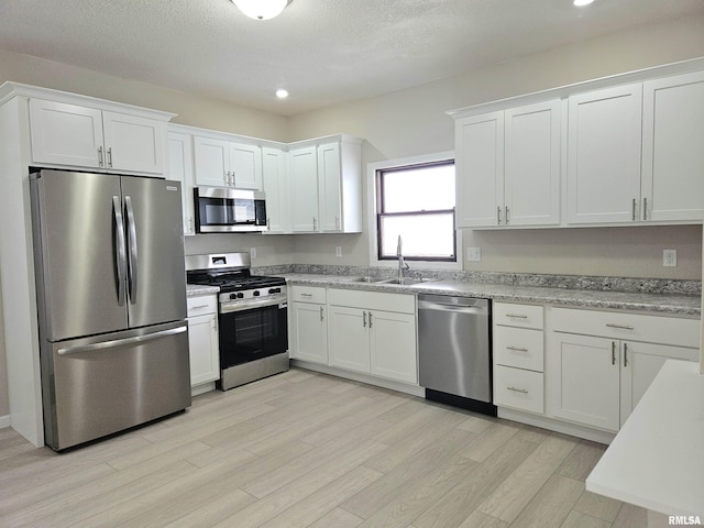 kitchen featuring recessed lighting, light wood finished floors, a sink, white cabinetry, and appliances with stainless steel finishes