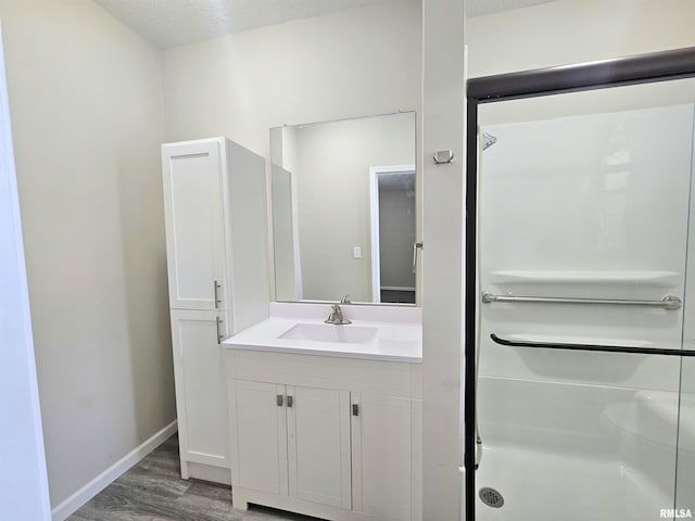 bathroom with a stall shower, baseboards, vanity, and wood finished floors
