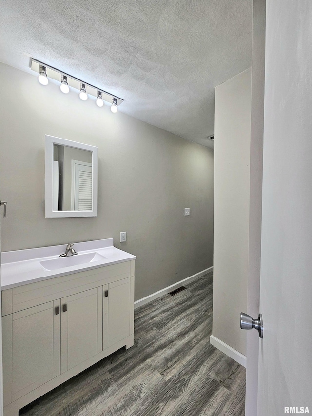 bathroom with a textured ceiling, visible vents, wood finished floors, and baseboards