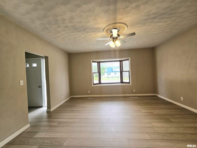 empty room featuring a ceiling fan, baseboards, a textured ceiling, and hardwood / wood-style flooring