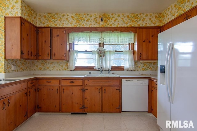 kitchen with a sink, brown cabinetry, white appliances, and wallpapered walls