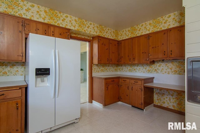 kitchen with wallpapered walls, white refrigerator with ice dispenser, and brown cabinetry
