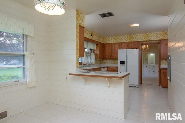 kitchen featuring a peninsula, brown cabinets, visible vents, white appliances, and light countertops