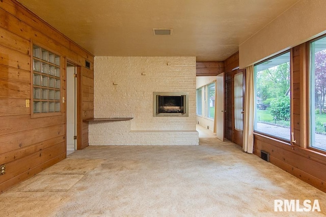 unfurnished living room with wooden walls, a brick fireplace, visible vents, and carpet