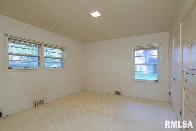 spare room featuring light colored carpet, visible vents, and a healthy amount of sunlight