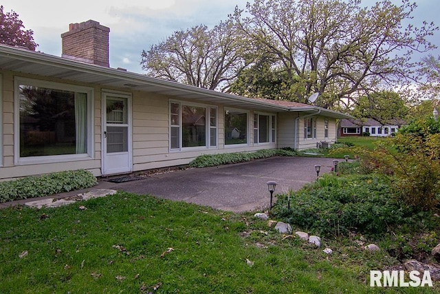 back of property featuring a patio, a chimney, and a lawn