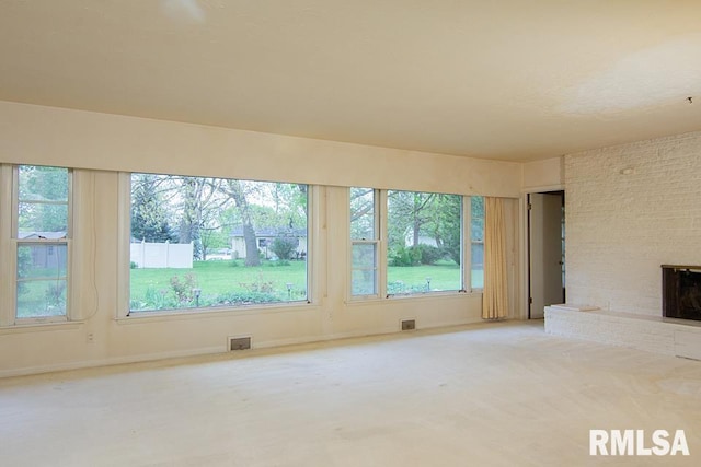 unfurnished living room with carpet flooring, plenty of natural light, visible vents, and a brick fireplace