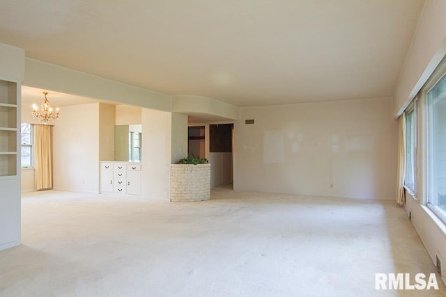 empty room with an inviting chandelier, light colored carpet, and plenty of natural light