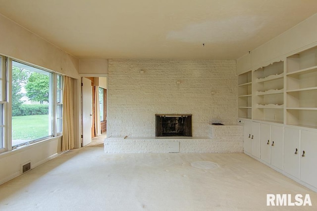 unfurnished living room featuring light carpet, a brick fireplace, and a healthy amount of sunlight