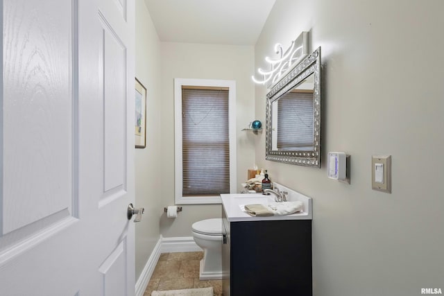 bathroom featuring vanity, toilet, baseboards, and stone finish flooring