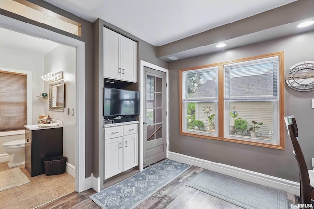 kitchen featuring white cabinetry, baseboards, light countertops, and wood finished floors