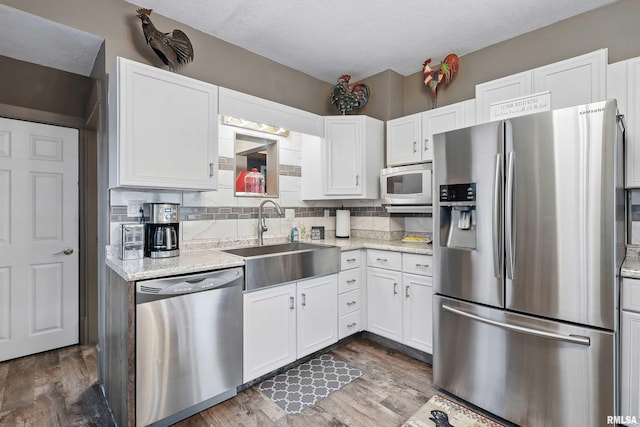 kitchen featuring wood finished floors, a sink, white cabinetry, appliances with stainless steel finishes, and decorative backsplash