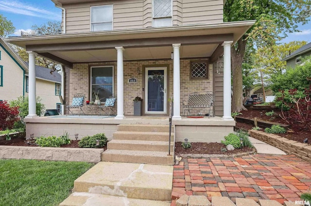 entrance to property with a porch and brick siding