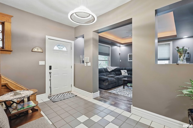 tiled foyer entrance featuring baseboards and a raised ceiling