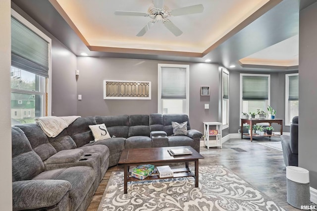 living room with a tray ceiling, wood finished floors, baseboards, and ceiling fan