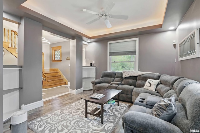 living area with baseboards, a raised ceiling, stairway, and light wood finished floors