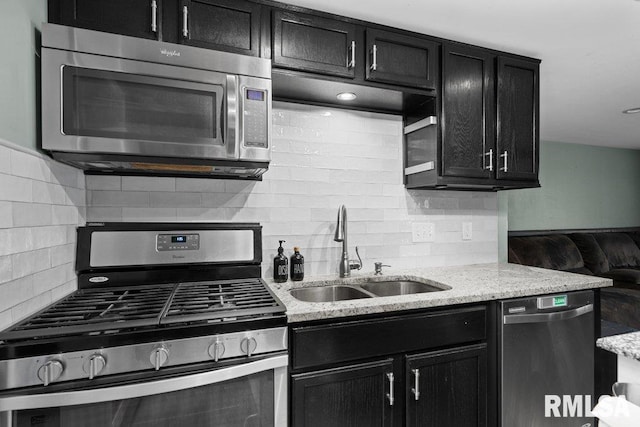 kitchen featuring dark cabinetry, light stone counters, a sink, stainless steel appliances, and tasteful backsplash