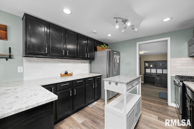 kitchen featuring light wood-type flooring, dark cabinets, tasteful backsplash, and stainless steel appliances