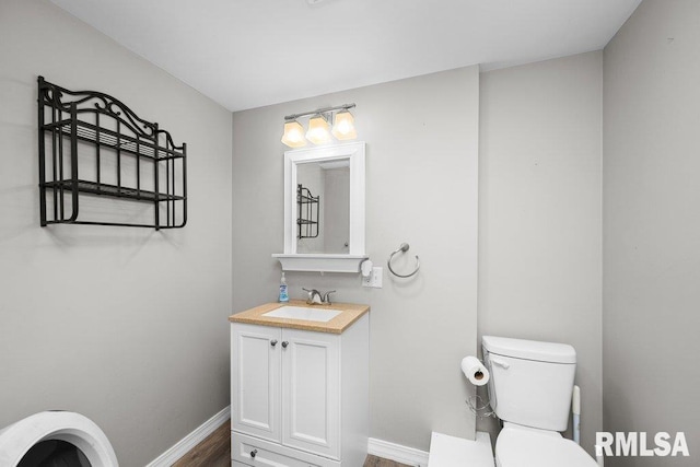 half bath with toilet, baseboards, vanity, and wood finished floors
