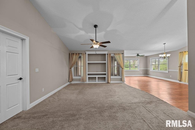 unfurnished living room featuring a textured ceiling, baseboards, carpet floors, and ceiling fan with notable chandelier