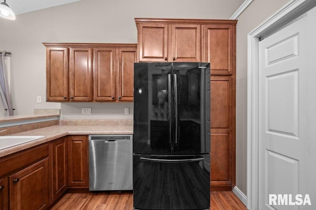 kitchen featuring freestanding refrigerator, brown cabinetry, stainless steel dishwasher, and light wood-style floors