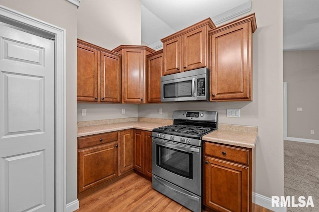 kitchen with brown cabinets, light wood-style floors, baseboards, light countertops, and appliances with stainless steel finishes