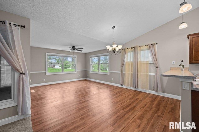 unfurnished living room with a textured ceiling, baseboards, ceiling fan with notable chandelier, vaulted ceiling, and wood finished floors