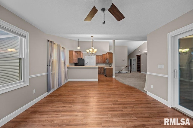 unfurnished living room with light wood-style flooring, ceiling fan with notable chandelier, a textured ceiling, baseboards, and vaulted ceiling