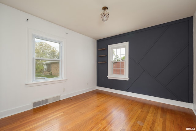 empty room featuring light wood-style flooring, a wealth of natural light, baseboards, and visible vents