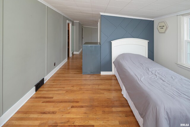 bedroom with baseboards, light wood finished floors, crown molding, and visible vents
