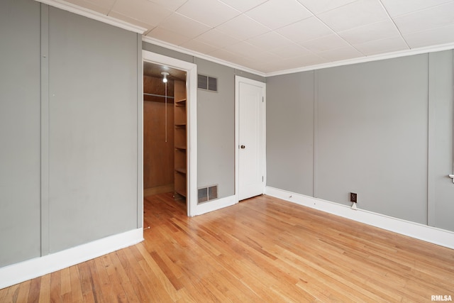 unfurnished bedroom featuring crown molding, light wood-type flooring, visible vents, and a walk in closet