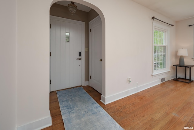 foyer entrance with arched walkways, baseboards, visible vents, and wood finished floors