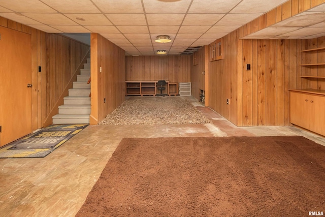 finished basement with a paneled ceiling, wooden walls, and stairs