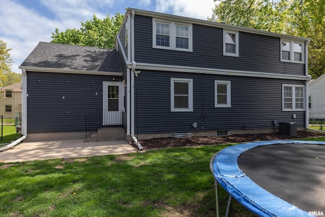 rear view of property featuring a patio area, a trampoline, entry steps, cooling unit, and a lawn