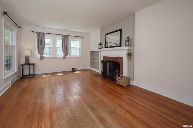 unfurnished living room with baseboards, a fireplace, visible vents, and wood finished floors