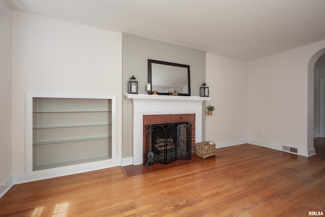 unfurnished living room with arched walkways, baseboards, a fireplace, and wood finished floors