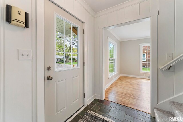 entryway with crown molding, stone tile flooring, and baseboards