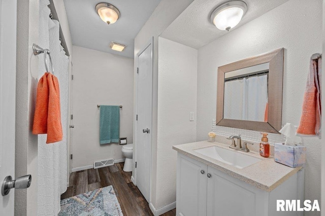 bathroom with toilet, wood finished floors, visible vents, baseboards, and vanity