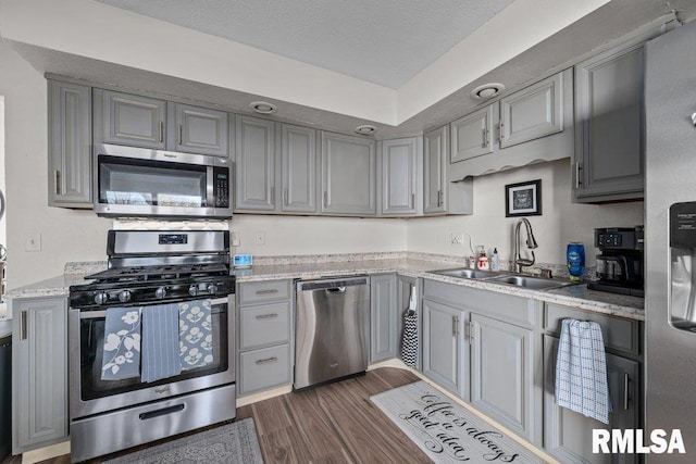 kitchen with light stone countertops, dark wood finished floors, a sink, appliances with stainless steel finishes, and gray cabinets