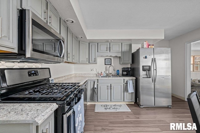 kitchen featuring stainless steel appliances, light wood-type flooring, a sink, and gray cabinets