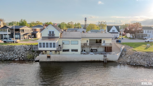 back of house featuring metal roof, a sunroom, a water view, and a residential view