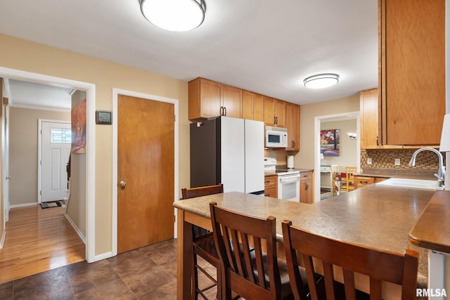 kitchen with white appliances, a sink, tasteful backsplash, a kitchen breakfast bar, and a peninsula
